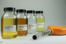 Vier Laborflaschen mit unterschiedlich farbigen Flüssigkeiten transparent bis dunkelgelb stehen neben einer Zapfpistole.
