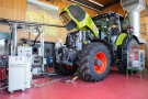 Hellgrüner Traktor mit roten Felgen auf dem Prüfstand mit geöffneter Motorhaube umgeben von Analysegeräten.