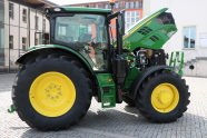 On a cloudy day, in foreground a John Deere 6135R project tractor with buildings in the background.