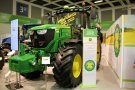 A tractor of the John Deere company is displayed with a front weight and a decal “Pflanzenöl” (Plant oil) on its windscreen in an exhibition hall.