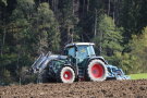 Fendt-Traktor eggt Acker, im nahen Hintergrund Nadelwald