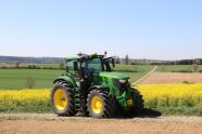 A green tractor with yellow rims on a track in front of a yellow rapeseed field amidst fields