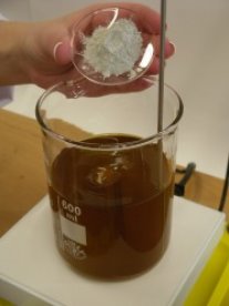 Zudosierung eines pulverförmigen Zuschlagstoffes in ein Becherglas, das Rapsölkraftstoff enthält.