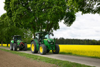 Zwei Rapsöl-Traktoren fahren auf einer Landstraße an einem Rapsfeld vorbei 