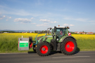 Traktor fährt auf einer Landstraße, im Hintergrund ist ein Rapsfeld zu sehen