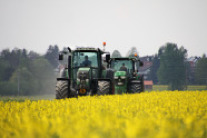 Zwei Traktoren fahren an einem Rapsfeld entlang