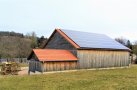 Das Foto zeigt einen großen Holzschuppen mit Photovoltaikanlage auf dem Dach