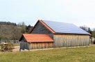 Das Foto zeigt einen großen Holzschuppen mit Photovoltaikanlage auf dem Dach