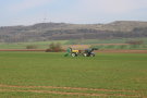 Das Foto zeigt einen blauen Traktor mit gelbem Güllefass mit Schleppschläuchen bei der Gärrestausbringung.