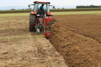 Das Foto zeigt einen roten Traktor beim Pflügen des Ackers.