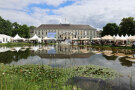 Gebäude im Hintergrund, Zelte auf Wiese und See im Vordergrund