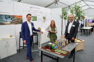 Zwei Männer und eine Frau stehen vor einem Messestand und lächeln in die Kamera