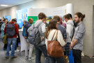Viele junge Menschen stehen vor einem Messestand und unterhalten sich
