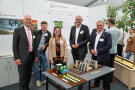 Vier Männer und eine Frau stehen vor einem Messestand und lächeln in die Kamera