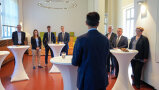 Personen stehen an Stehtischen und blicken auf Bundesminister Cem Özdemir