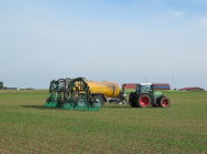 Ein Traktor zieht ein Fass mit vielen grünen Schläuchen über ein Feld