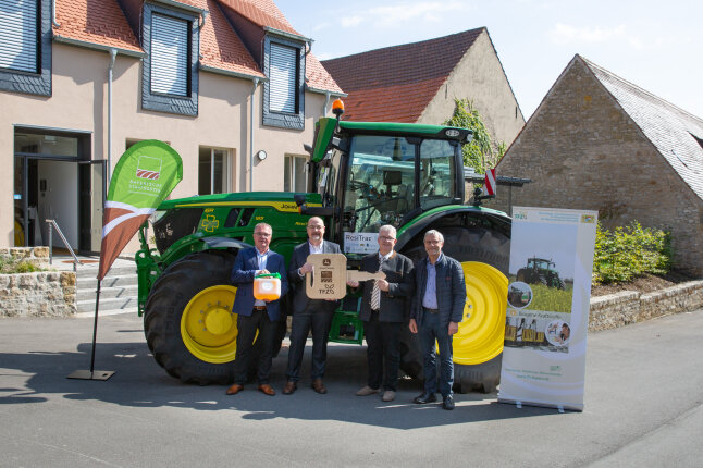 Vier Personen stehen vor einem grünen Traktor