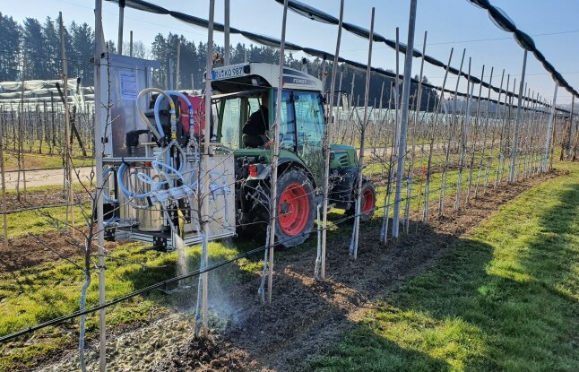 Ein Traktor spritzt eine Flüssigkeit entlang des Unterstockbereichs von Bäumen auf