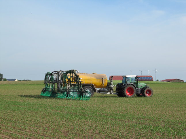  Ein Traktor zieht ein Fass mit vielen grünen Schläuchen über ein Feld