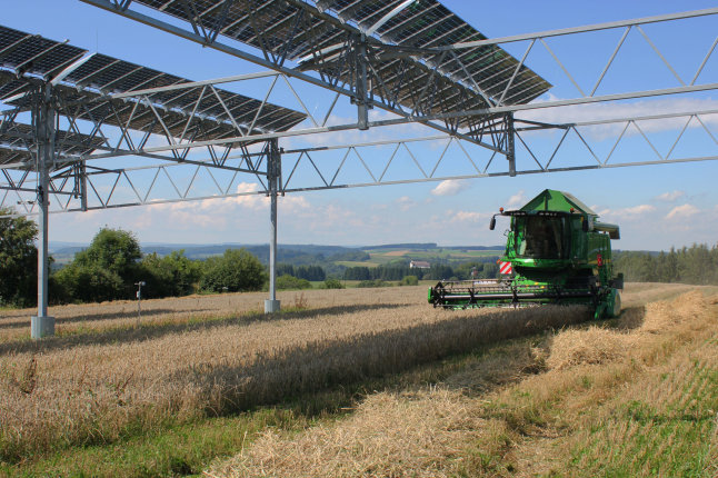 Mähdrescher drischt auf einem Feld unter einer Photovoltaik-Anlage