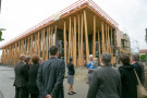 Eine Besuchergruppe steht vor der Baustelle des Nawareum, einem Museum in Holzbauweise mit Baumstämmen, die die Fassade zieren.