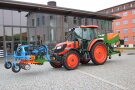 Oranger Traktor mit hinten und vorne einem Anbaugerät steht vor dem TFZ-Technikum.