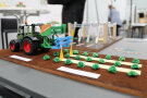 Miniatur-Modell mit Traktor mit grünem Anbaugerät steht auf braunen Boden vor 3-D-Kunststoff-Salatköpfen. von 