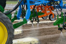 Traktor mit Spritzdüsen-Anbaugerät bringt gelben und weißen Sprühstrahl auf Acker aus.