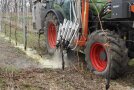 Ein Fendt-Traktor mit seitlichem Anbau von Düsen spritzt weißes Material im Weinberg.