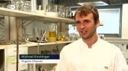 Ein Wissenschaftler mit weißem Kittel steht in einem Analytik-Labor und spricht in eine Kamera