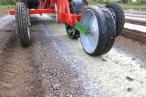 Anbaugerät rollt über Acker entlang eines weiß-gelben Materialstreifens