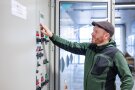 Mann steht vor grauem Kasten mit roten und grünen Knöpfen