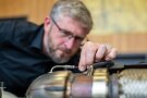 Mann inspiziert rote und blaue Kabel am Motorblock eines Traktors