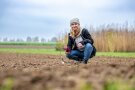 Frau kniet mit Gerät in der Hand am Feld